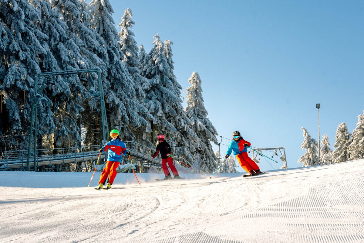 3 Kinder fahren auf der Wasserkuppe die Piste hinab