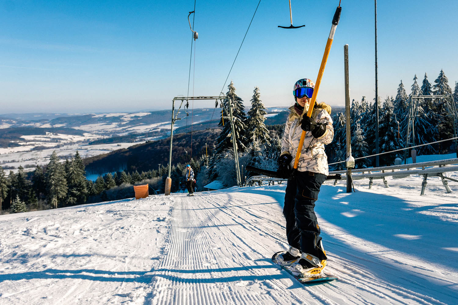 Snowboarderin fährt mit ihrem Snowboard im Schlepplift auf der Wasserkuppe nach oben.